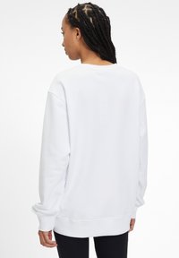 Felpa bianca con vestibilità comoda, spalle scese, polsini e orlo a costine. Tessuto morbido, design minimalista senza decorazioni.