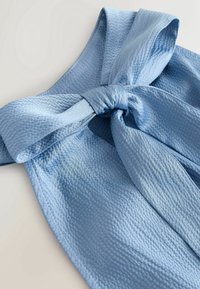 Gros plan d'une ceinture en tissu texturé bleu clair nouée en nœud sur un vêtement assorti.