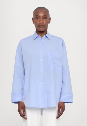 Camicia a righe blu chiaro con colletto, maniche lunghe e taschino sul petto con sottili righe verticali. Chiusura frontale con bottoni e dettaglio ai polsini.