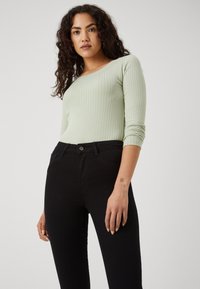 Light green ribbed long-sleeve top paired with black fitted jeans. The top features a scoop neckline and textured fabric.