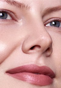 Närbild av ett ansikte med jämn hy, ljusa rodnadstoner och matt rosa läppstift. Ögonen är klara med naturliga ögonfransar och välvårdade ögonbryn.