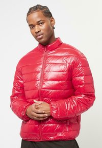 Rote Steppjacke aus glänzendem Material, mit horizontalen Quiltnähten, einem hohen Kragen und einem Reißverschluss vorne. Leichtgewichtig und warmes Design.