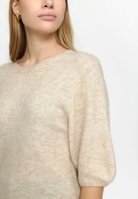 Beige gebreide trui met een ronde hals, korte pofmouwen en een zachte, gestructureerde afwerking. Lichte, luchtige stof met een subtiel patroon.