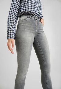 Jeans skinny de denim cinza com um corte de cintura alta, apresentando um fecho de cinco botões, bolsos frontais e um ligeiro desbotado no tecido.