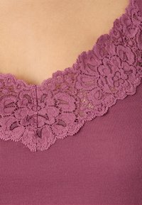Purple top featuring a floral lace neckline with intricate details, complemented by a ribbed texture on the body.