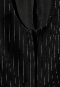 Țesătură neagră cu dungi verticale subțiri albe și un decolteu adânc, rotunjit, evidențiind un detaliu al cusăturii frontale în centrul bluzei.