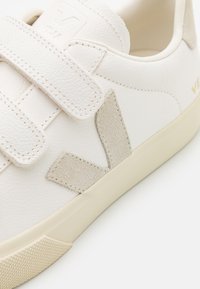 Baskets en cuir blanc avec des accents en daim beige. Dotées de bandes velcro et d'une semelle en caoutchouc texturé. Logo de la marque visible sur la languette.