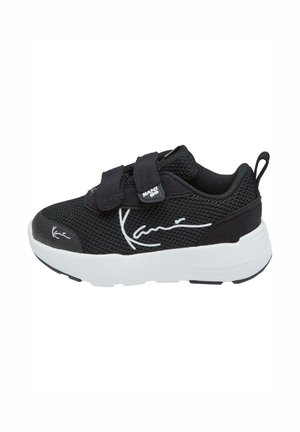 Chaussure de sport noire avec tige en mesh, double bandoulière Velcro, semelle blanche et accents de logo blancs bien visibles sur le côté et la languette.