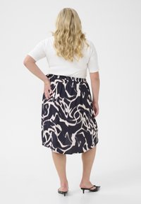 Gonna fluida stampata con swirl astratti in bianco e nero, vita elastica, lunghezza al ginocchio, realizzata in tessuto leggero. Tacchi neri classici.