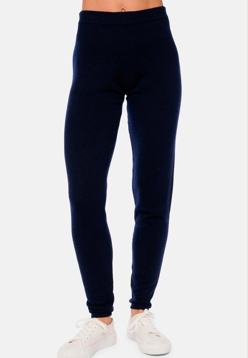 Modèle portant des leggings ajustés bleu marine associés à des baskets blanches, sur un fond léger uni. Accent sur le confort et le style.