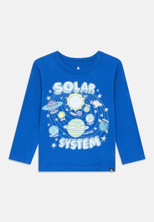 Kék hosszú ujjú ing, amelyen egy naprendszer grafika látható: a Nap, a bolygók feliratozva, és egy űrrepülőgép, amely kering körülöttük.