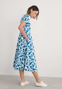 Blue and white printed dress with short sleeves, knee-length, A-line shape, featuring a geometric pattern and side pockets. Worn with white sneakers.