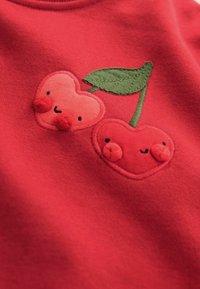 Rotes Sweatshirt mit gestickten herzförmigen Kirschen in hell- und dunkelrot, mit grünen Blättern und kleinen, strukturierten Akzenten.