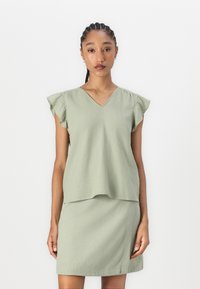 Top verde leggero con maniche ruffle corte e scollatura a V, abbinato a una gonna verde coordinata. Texture liscia, design casual.