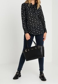 Sac à main noir en matériau lisse, avec des finitions en or, un design structuré, des poignées doubles et des accents métalliques.
