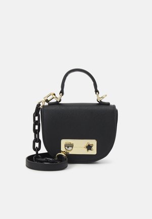 Černá kožená kabelka s krátkým uchem, zlatým obdélníkovým zapínáním s motivem oka a hvězdy a černým řetízkovým popruhem stočeným vedle ní.