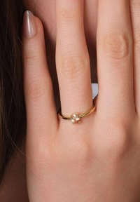 Goldring mit einem kleinen, klaren Edelstein in einem minimalistischen Design. Die Hand hat einen hellen Hautton und gepflegte Nägel.