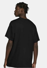 Tricou din bumbac negru cu mâneci scurte și o croială relaxată. Articolul prezintă un guler rotund și o textură fină.