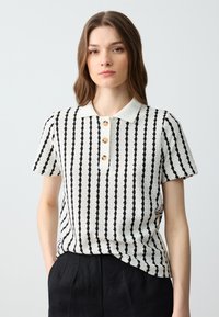 Polo à manches courtes noir et blanc rayé avec un motif en tricot texturé et trois boutons au col. Col blanc uni.