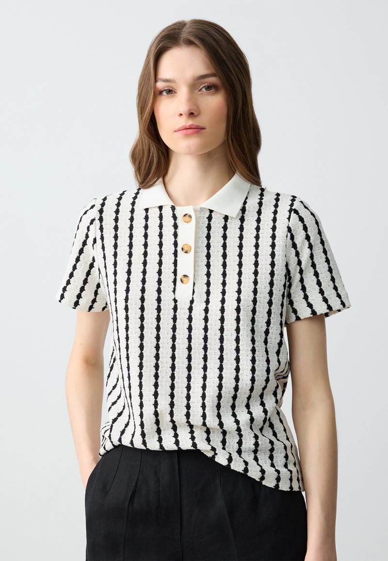 Polo à manches courtes noir et blanc rayé avec un motif en tricot texturé et trois boutons au col. Col blanc uni.