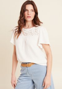 Witte blouse met korte mouwen van textuurstof, met een kant yoke ontwerp. Gecombineerd met lichtblauwe high-waisted jeans en een tan riem.