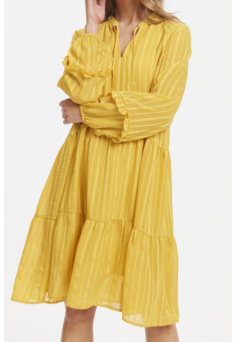 Robe jaune à étages en tissu léger à rayures verticales. Caractérisée par des manches longues avec des poignets à volants et un col en V discret.