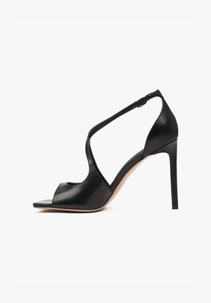 Czarna skórzana sandałka na wysokim obcasie z otwartym noskiem, paskiem wokół kostki z klamrą oraz gładką, elegancką teksturą.