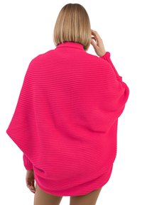 Poncho de punto rosa intenso con textura acanalada, con un corte holgado y mangas largas. La tela parece suave con un caída acogedora.