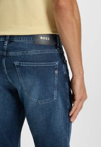 Mörkblå denimjeans med en läderpatch från BOSS på den bakre midjan, med femficksdesign och subtila sömnadsdetaljer.