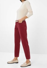 Pantalon en velours côtelé rouge avec jambes fuselées et poches latérales, associé à un haut à manches longues côtelé crème et des mocassins beiges.
