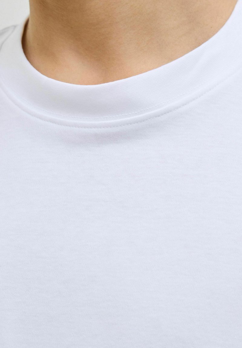 Tricou alb din bumbac cu guler rotund și mâneci scurte, având o textură netedă și detalii minime de coasere în jurul gulerului.