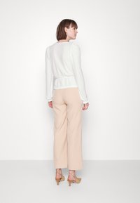 Camisa branca texturizada de mangas compridas com cintura ajustada, combinada com calças largas beijas de cintura alta e sapatos de salto bloco castanho claro com tiras.