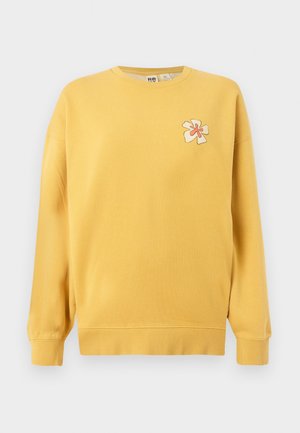 Gul genser laget av bomull, med rund hals og ribbestrikkede mansjetter. Bestickede blomsterdetaljer i lyse og mørke farger på brystet.