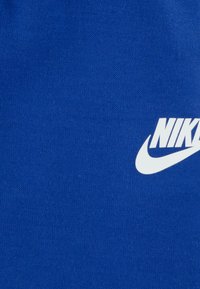 Blauer Stoff mit glatter Textur, auf dem in fetter Schrift das auffällige weiße Nike-Logo unten rechts zu sehen ist.