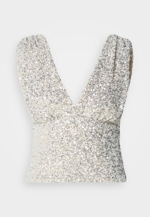 Sidabrinė blizganti be rankovių palaidinė su giliu V formos iškirpimu ir drapiruotomis pečių detalėmis. Lynnualus paviršius su spindinčiomis dekoracijomis visame paviršiuje.