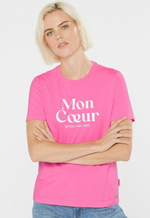 Bright pink t-shirt with short sleeves featuring white text "Mon Cœur" and "SENSES.THE LABEL". Soft fabric, relaxed fit, tag on side.