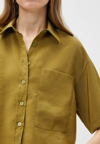 Olijfgroene short-sleeve shirt met een klassieke kraag, frontzak en knoopsluiting. Gladde stofstructuur en subtiele glans.