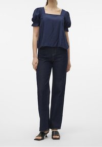 Mörkblå puffärmstop med fyrkantig halsringning, kombinerad med högmidjade mörk denim raka byxor och svarta klackskor med öppen tå.