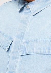 Light blue denim shirt featuring a pointed collar, two front pockets, button closures, and visible stitching details. Soft texture.