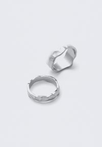 Deux bagues argentées aux bords ondulés irréguliers posées sur une surface blanche unie.
