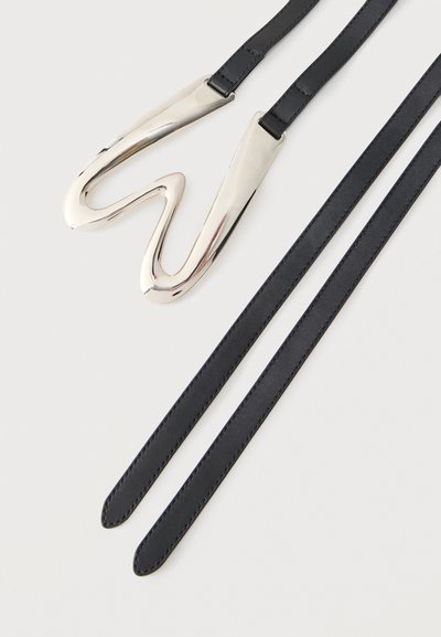 Μαύρη δερμάτινη ζώνη με λαμπερή ασημένια αφηρημένη κυματιστή αγκράφα σε λευκό φόντο.