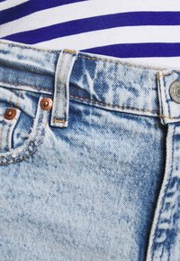 Jeans de mezclilla en un azul claro con una textura desgastada, con costuras visibles, un botón de metal y un cierre de botón superior en la cintura.