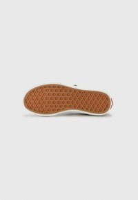 Semelle de sneaker avec une surface en caoutchouc gomme texturé, présentant un motif en diamant ; bord blanc et accent rouge au talon.