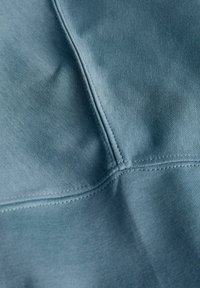 Texturált kivitelű, tompa kék árnyalatú szövet látható varrásokkal és öltésrészletekkel, sima, enyhén rugalmas megjelenéssel.