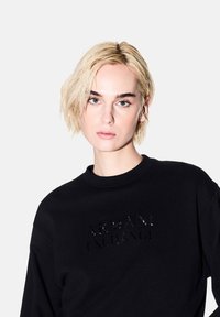 Felpa nera con colletto rotondo, caratterizzata da un logo lucido "Armani Exchange" al centro. Il tessuto sembra morbido con una vestibilità rilassata.