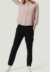 Blouse rose pâle à rayures avec boutons et manches trois-quarts ; associée à un pantalon noir fuselé et des baskets blanches.