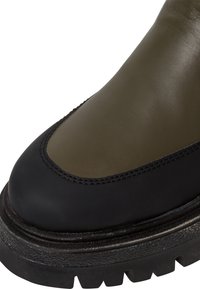 Olivgrüner Leder-Ankle-Boot mit einer schwarz gummierten Zehenkappe und dickem, strukturiertem Profil. Mit auffälligen Nähten entlang der Nähte.