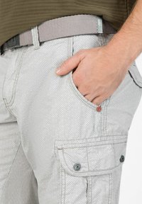 Light grey cargo shorts in textured fabric featuring a diamond pattern, side pockets, and a flat front pocket with buttons. Worn with a woven grey belt.