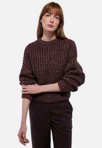 Pull en maille épaisse de couleur rouge foncé et noir, avec un col rond, une coupe décontractée et des poignets côtelés, associé à un pantalon tailleur.