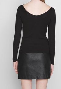 Zwarte geribbelde top met lange mouwen en V-hals, gecombineerd met een zwarte mini-rok van nep leer, met een gladde textuur en een aansluitende pasvorm.